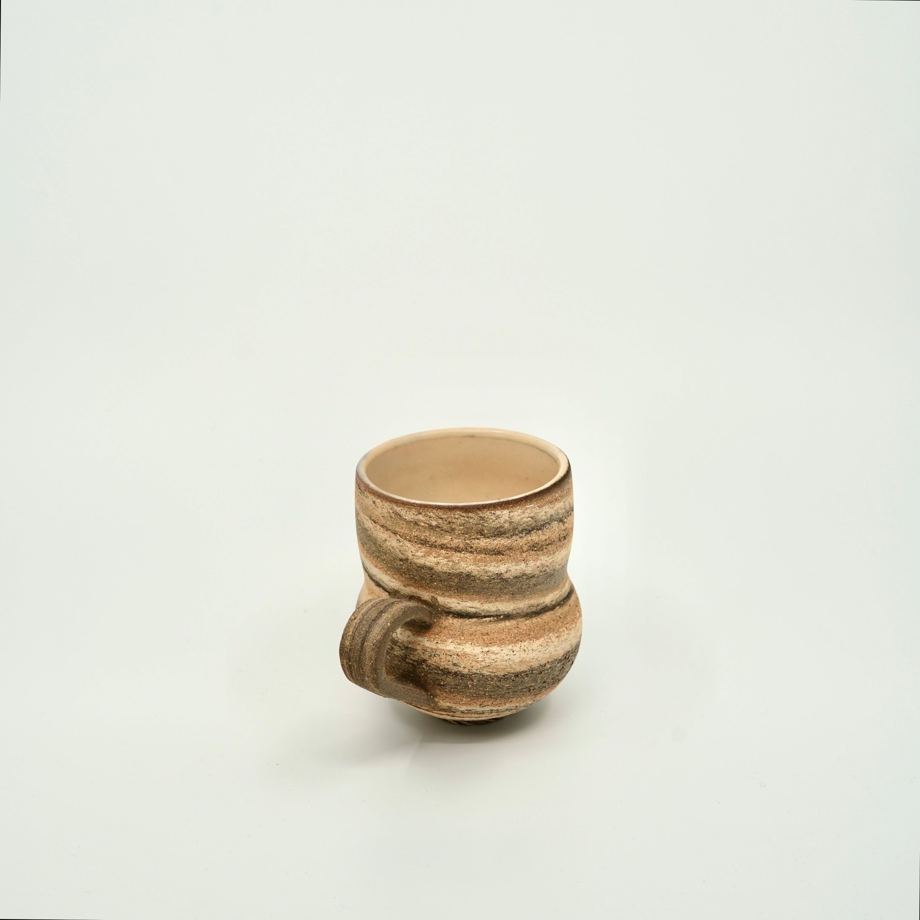 A small handmade ceramic cup by studio stream and crescent with a textured, ribbed surface and a protruding handle, shown on a plain light gray background.